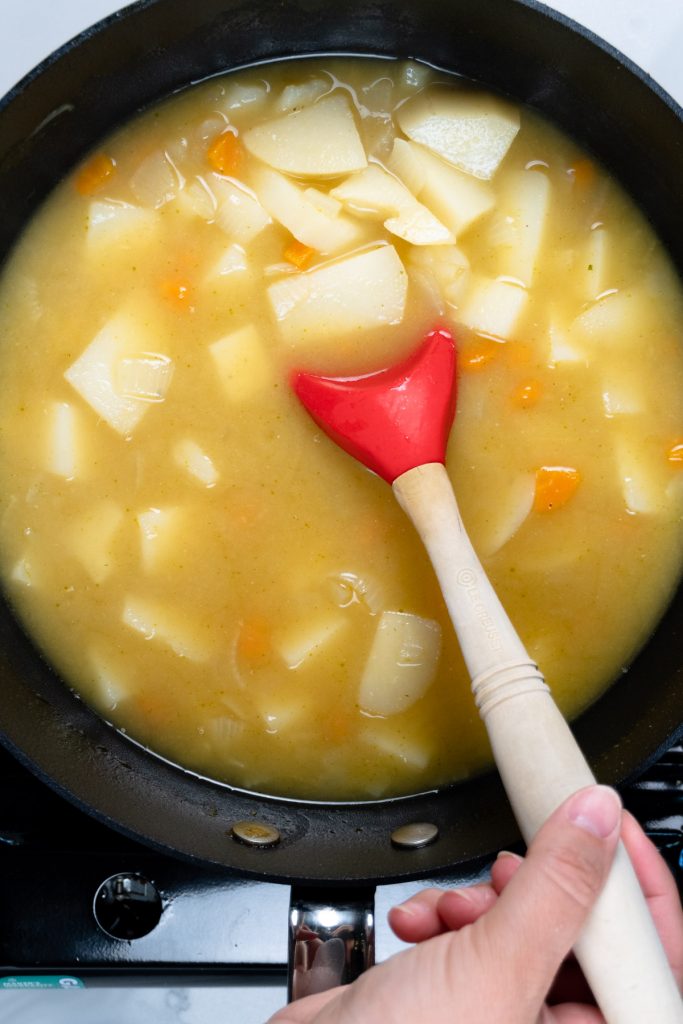 a red ladel in a black pot of potato soup