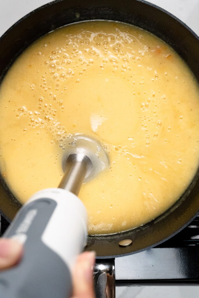 a stick blender in a pot blending yellowsoup