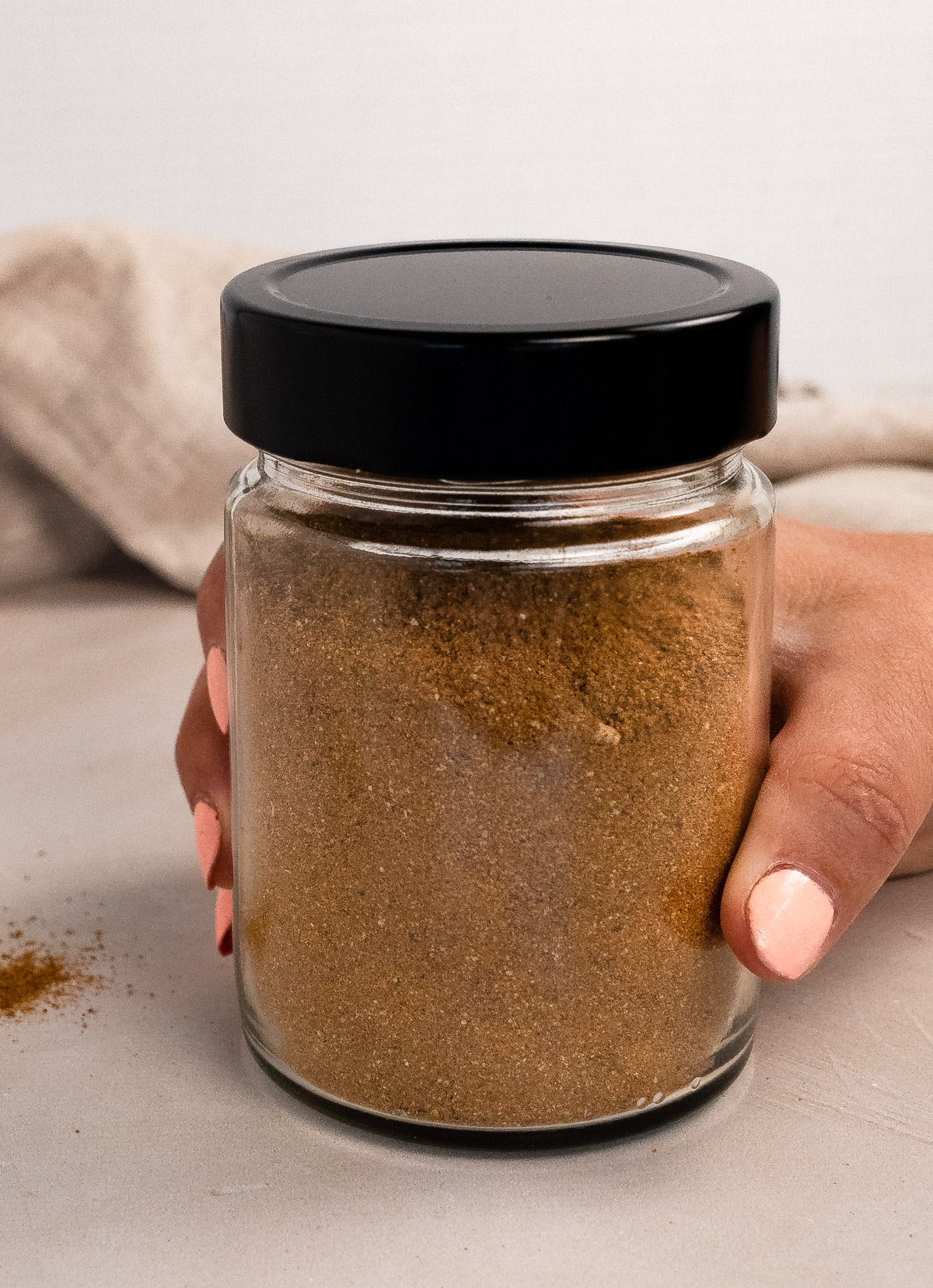 a female hand holding a jar of spices with a black lid