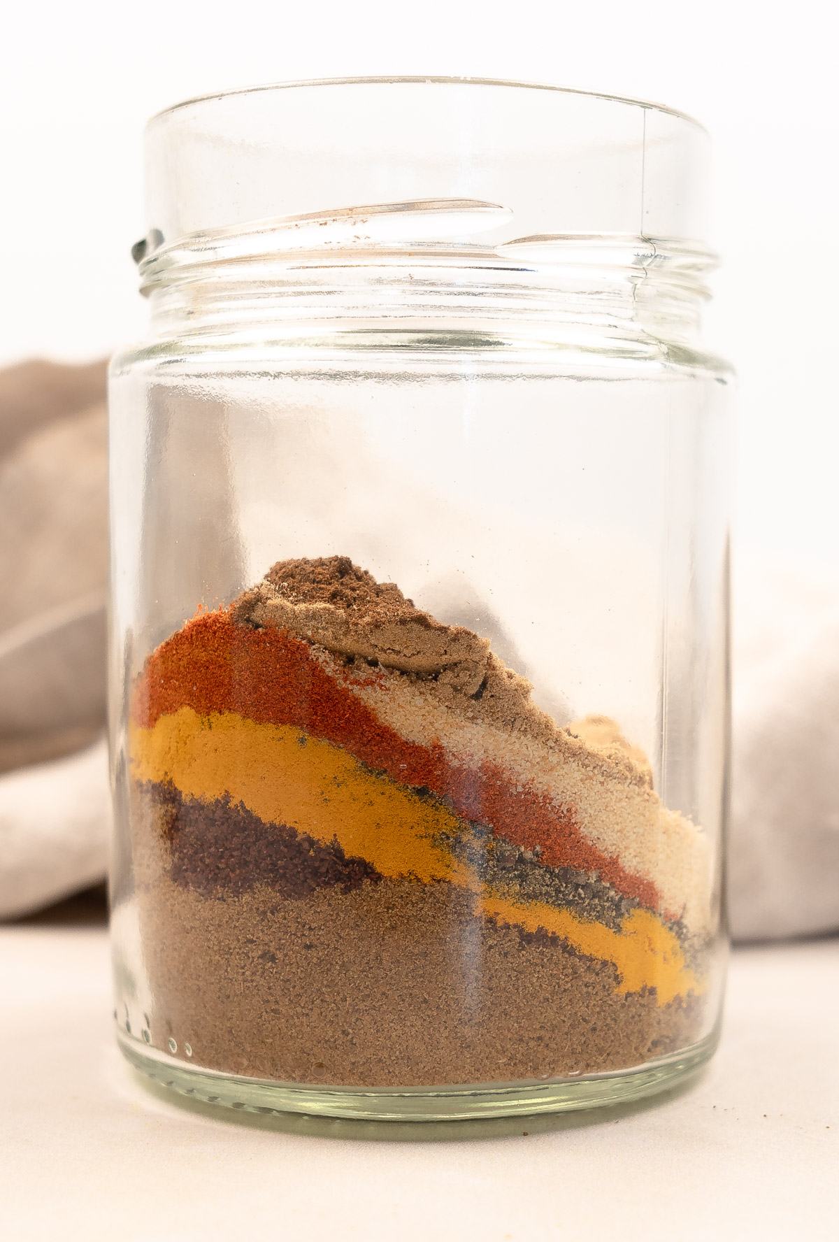 different coloured spices layered on top of each other in a clear jar