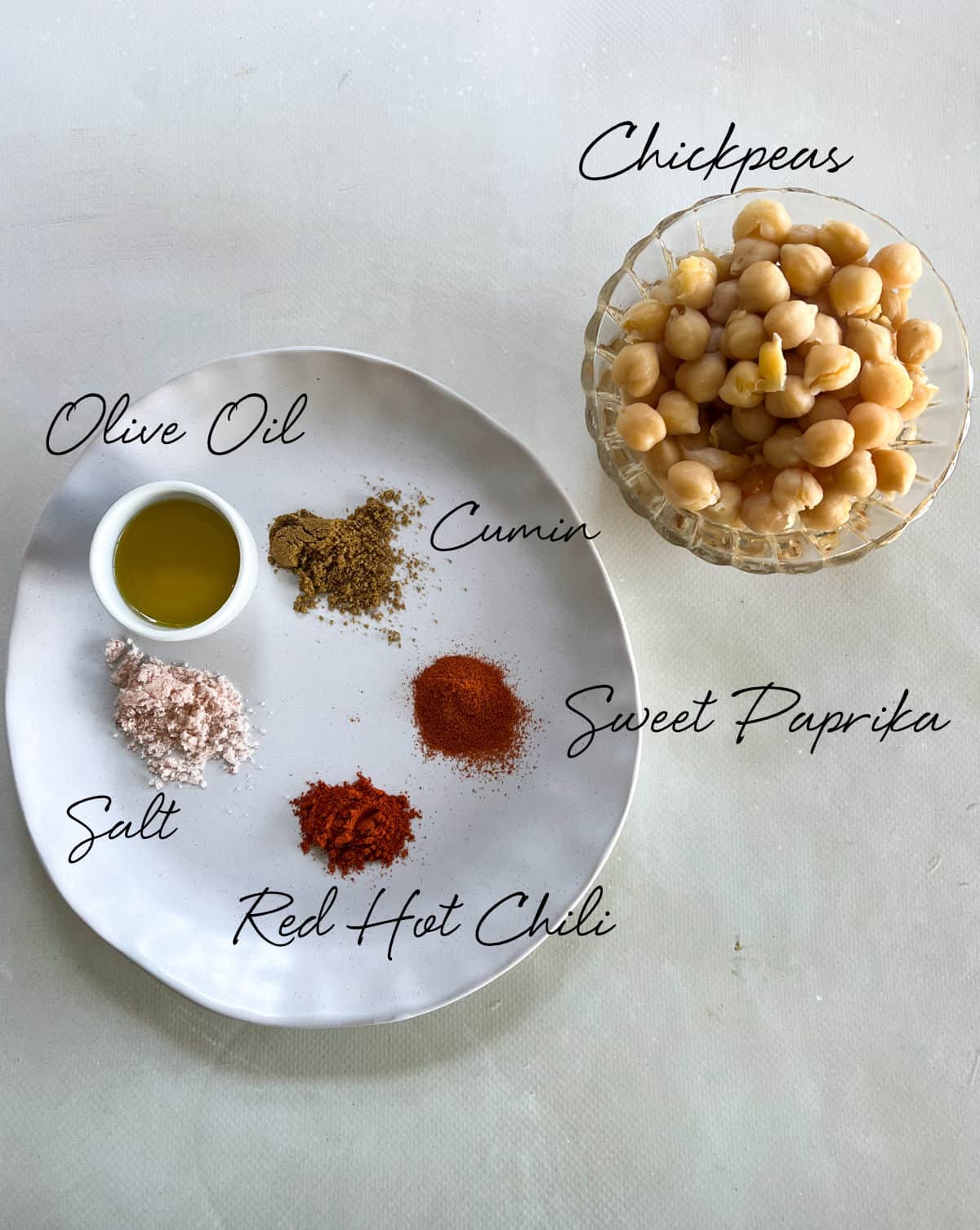 cooked chickpeas, olive oil, red chili, cumin, paprika and salt on a white plate