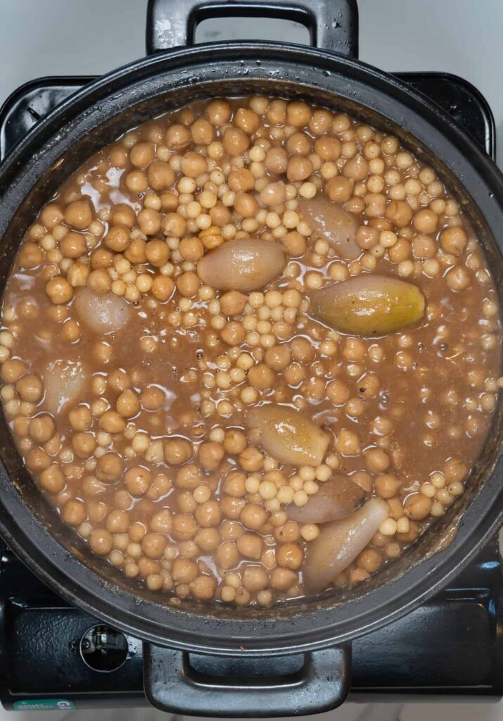 cooked pearl couscous, french shallots and chickpeas in a brown broth