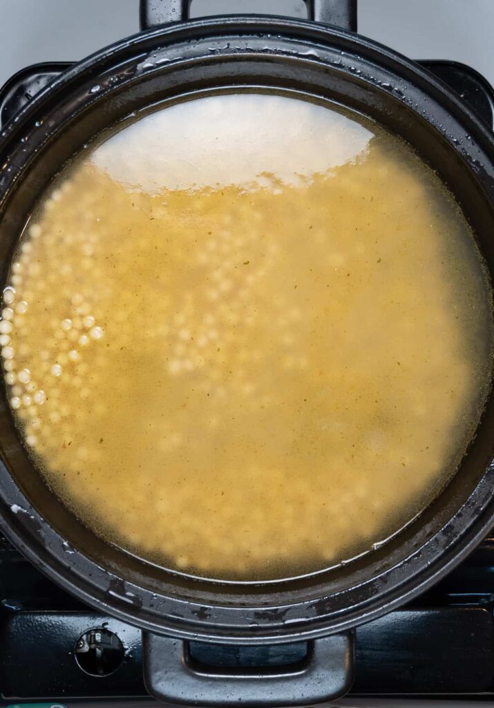 dry pearl couscous in vegetable stock in a black pan