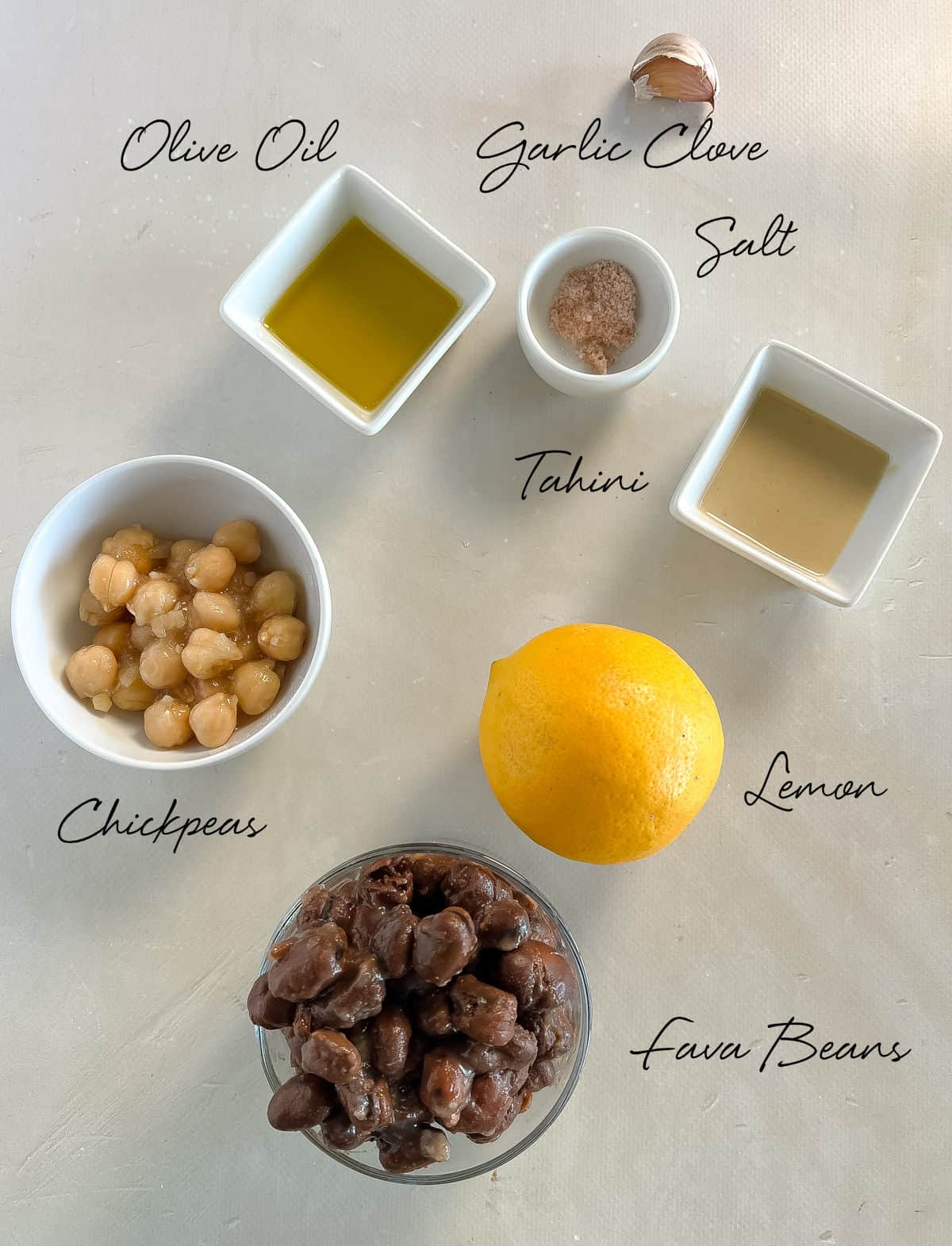 tahini, lemon, fava beans, chickpeas, olive oil, salt and garlic on a white bench top