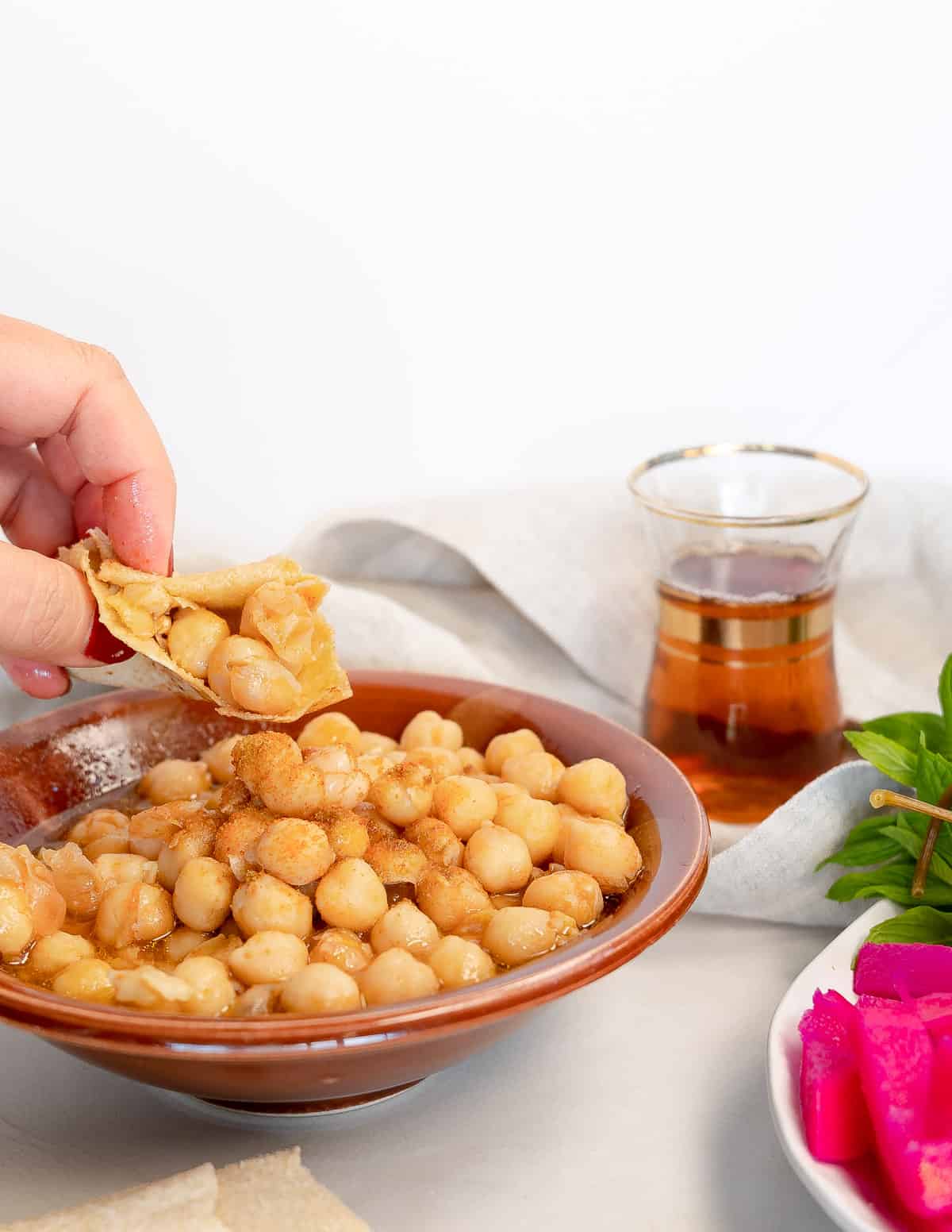 a hand holding garbanzo beans in a piece of bread over a brown bowl