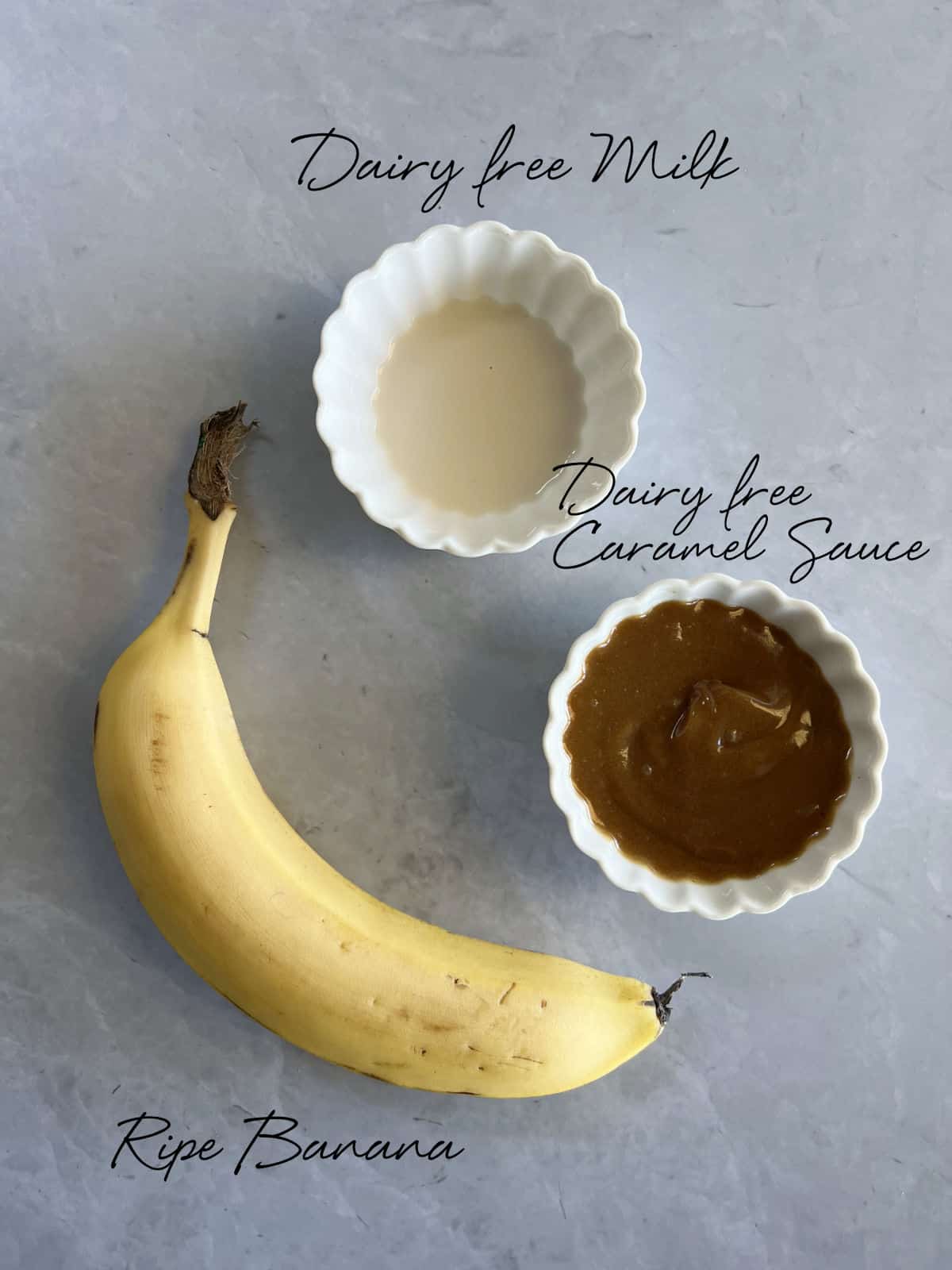 a ripe banana, milk and caramel in bowls on a grey benchtop