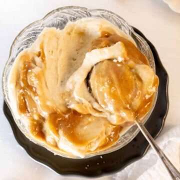 a glass bowl of nice cream topped with light brown saucewith a spoon in it