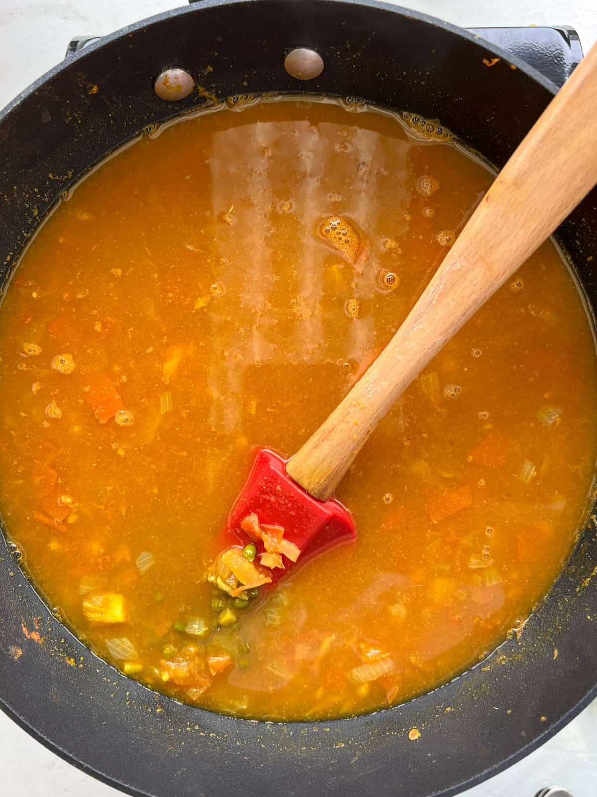 red water with mung beans and a red silicone spoon in a black sauce pan