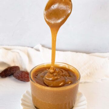 a small glass bowl filled with light brown caramel sauce with spoon dripping it in the bowl
