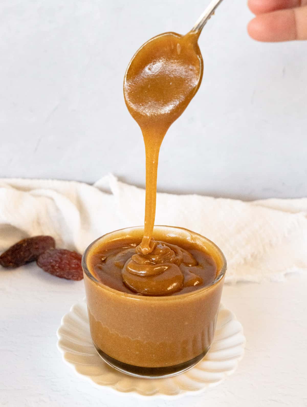 a small glass bowl filled with light brown caramel sauce with spoon dripping it in the bowl