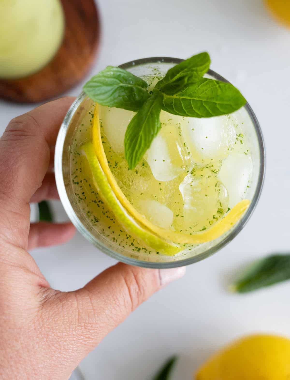 yellow juice with ice and bits of green flecks in a glass topped with mint leaves
