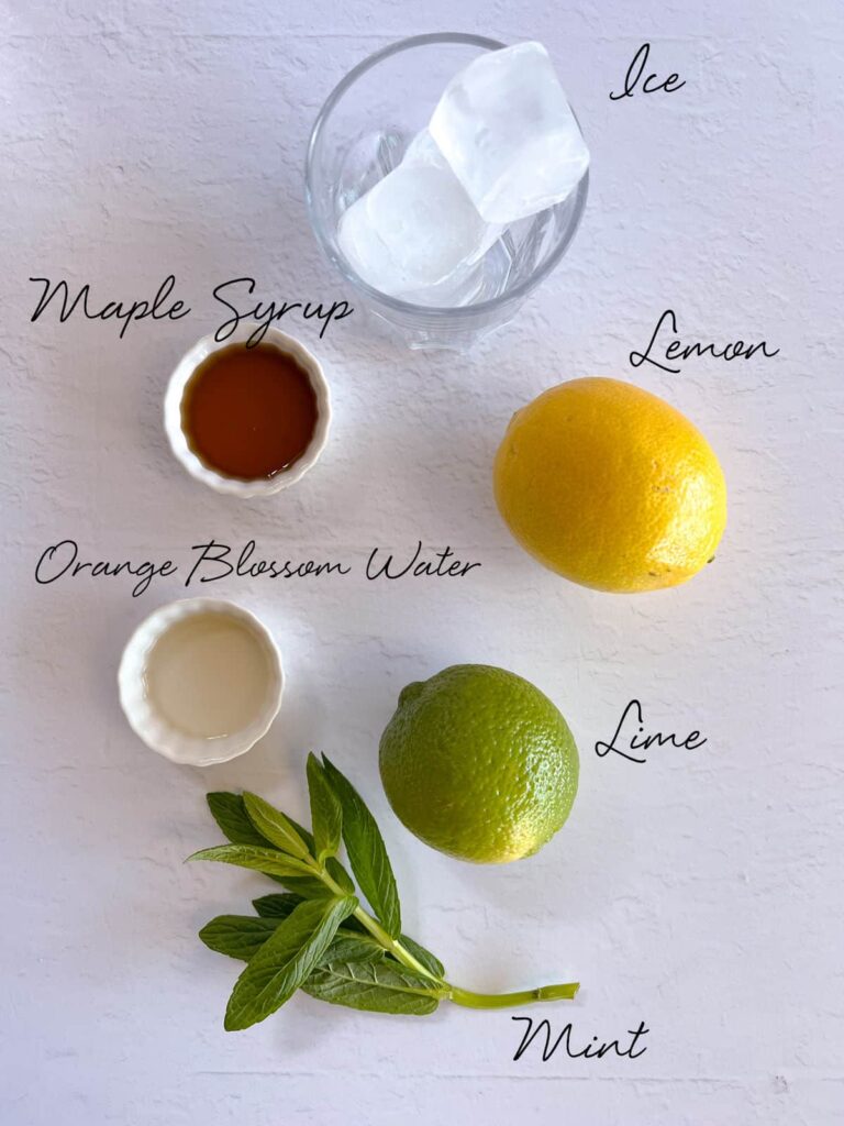 a lemon, lime, maple syrup, orange blossom water, ice and mint on a white bench
