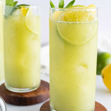 two tall glasses of yellow juice with slices of lime and lemon in them