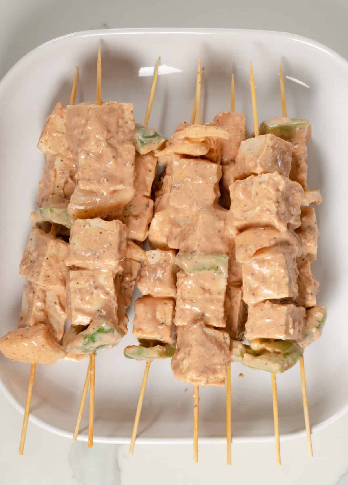 uncooked tofu skewers in a white square plate