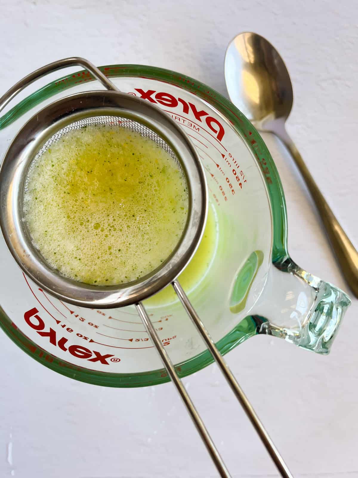 a strainer over a jug with yellow juice and bits of yellow lemon through it