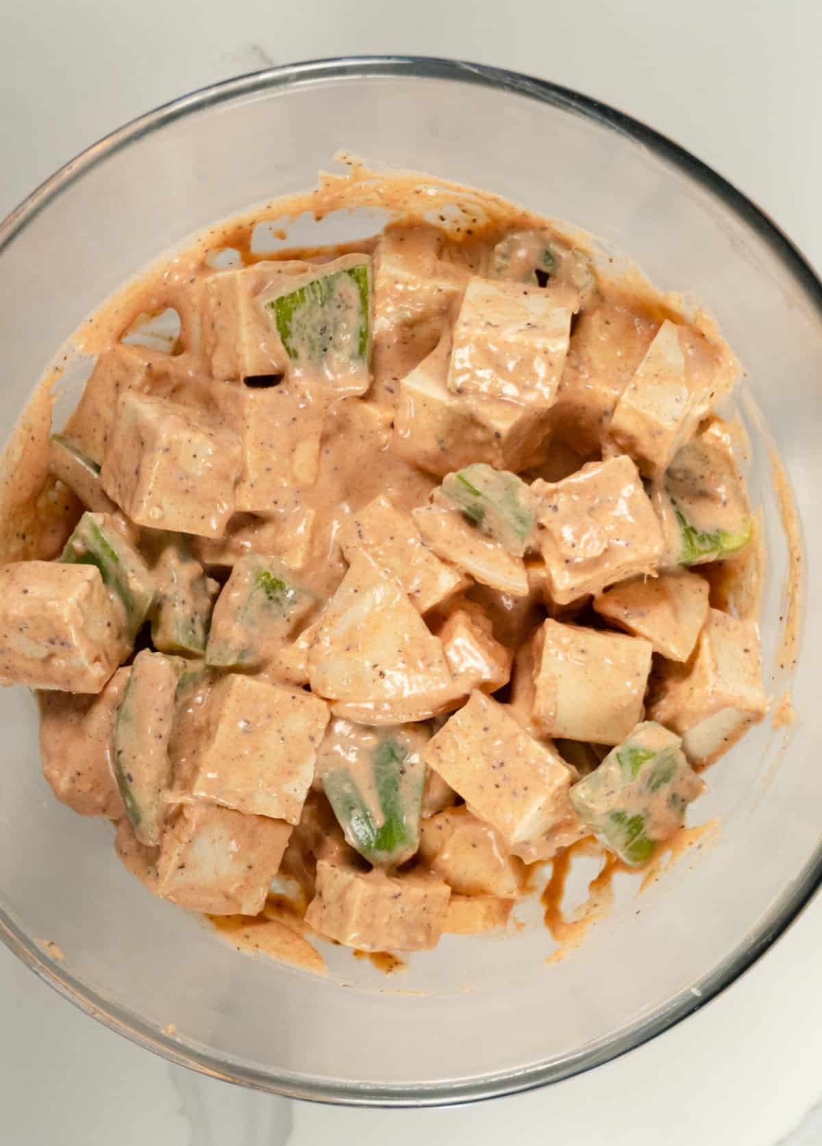 cubes of tufu, pieces of onion and pieces of capsicum in a pinkish sauce in a glass bowl