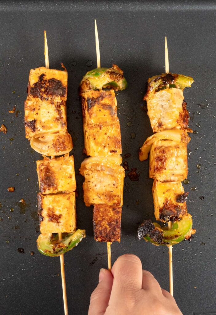 three skewers with tofu cubes and vegetables on a grill