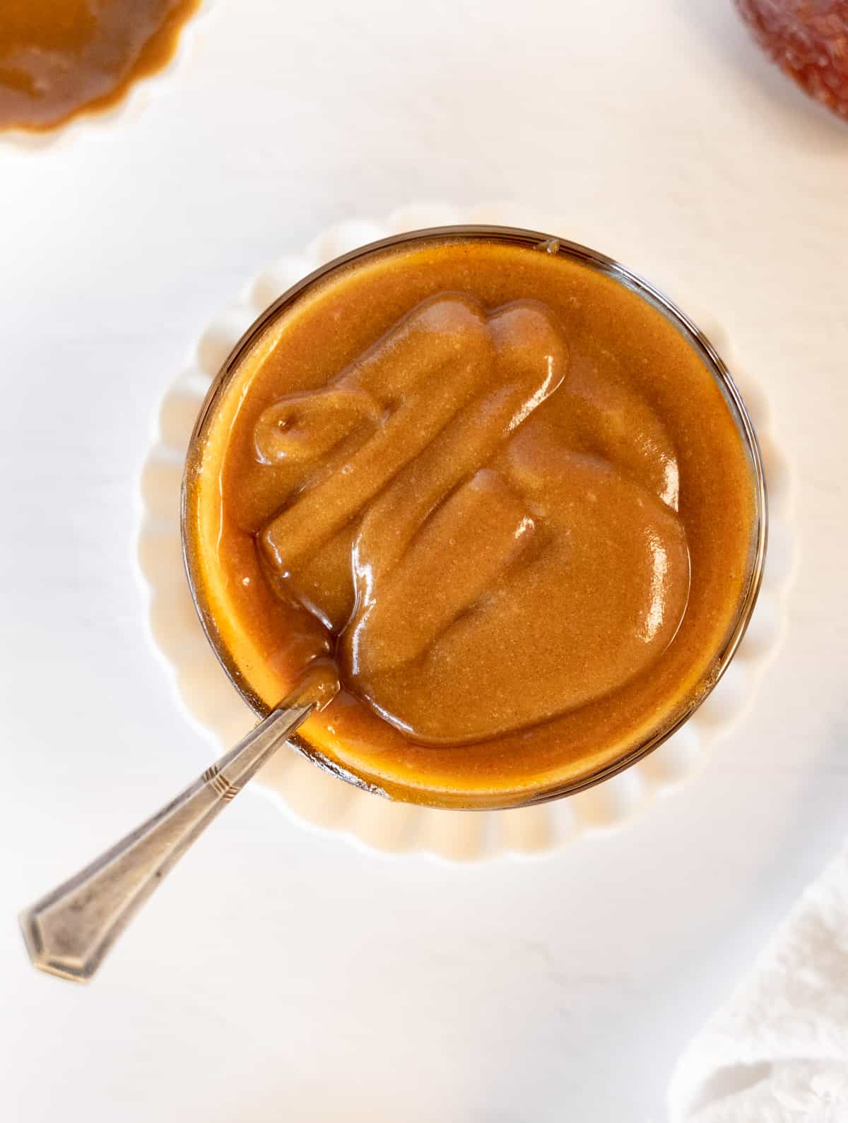 a bowl of light brown caramel sauce with a metal spoon in it