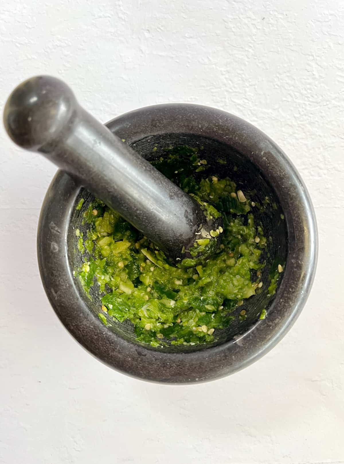 crushed green chili in a black mortar and pestle