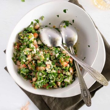 A white bowl of parsley salad with two silver spoons