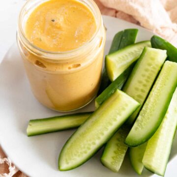 a glass jar of orange dressing with cucumber batons on the side
