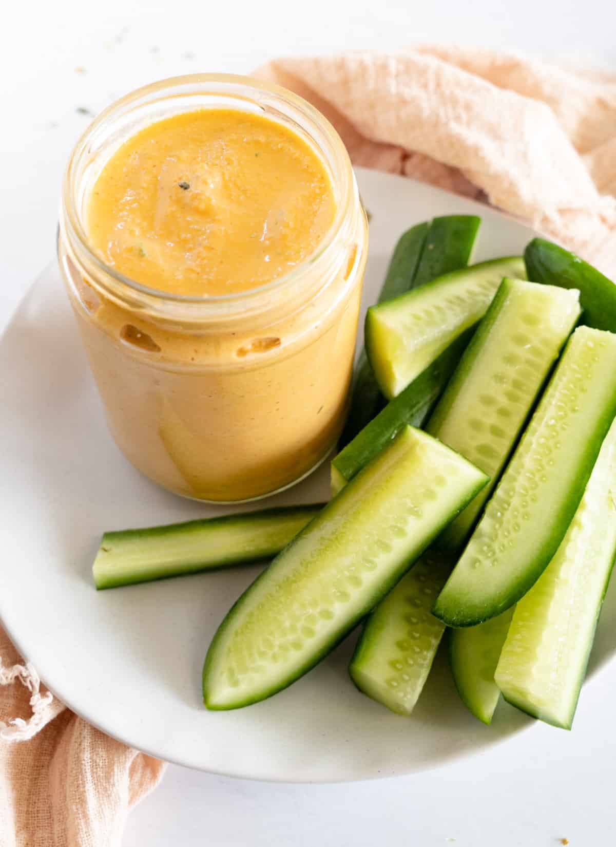 a glass jar of orange dressing with cucumber batons on the side