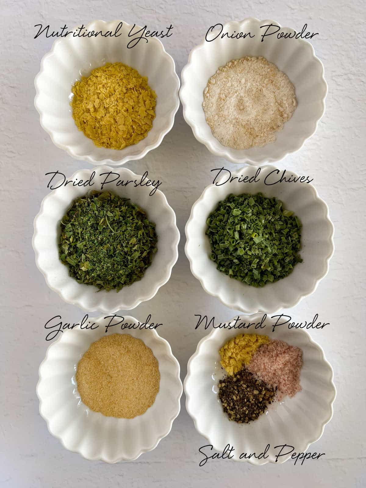 6 bowls containing nutritional yeast, onion powder, dried chives, dried parsley, garlic powder, mustard powder, salt and pepper