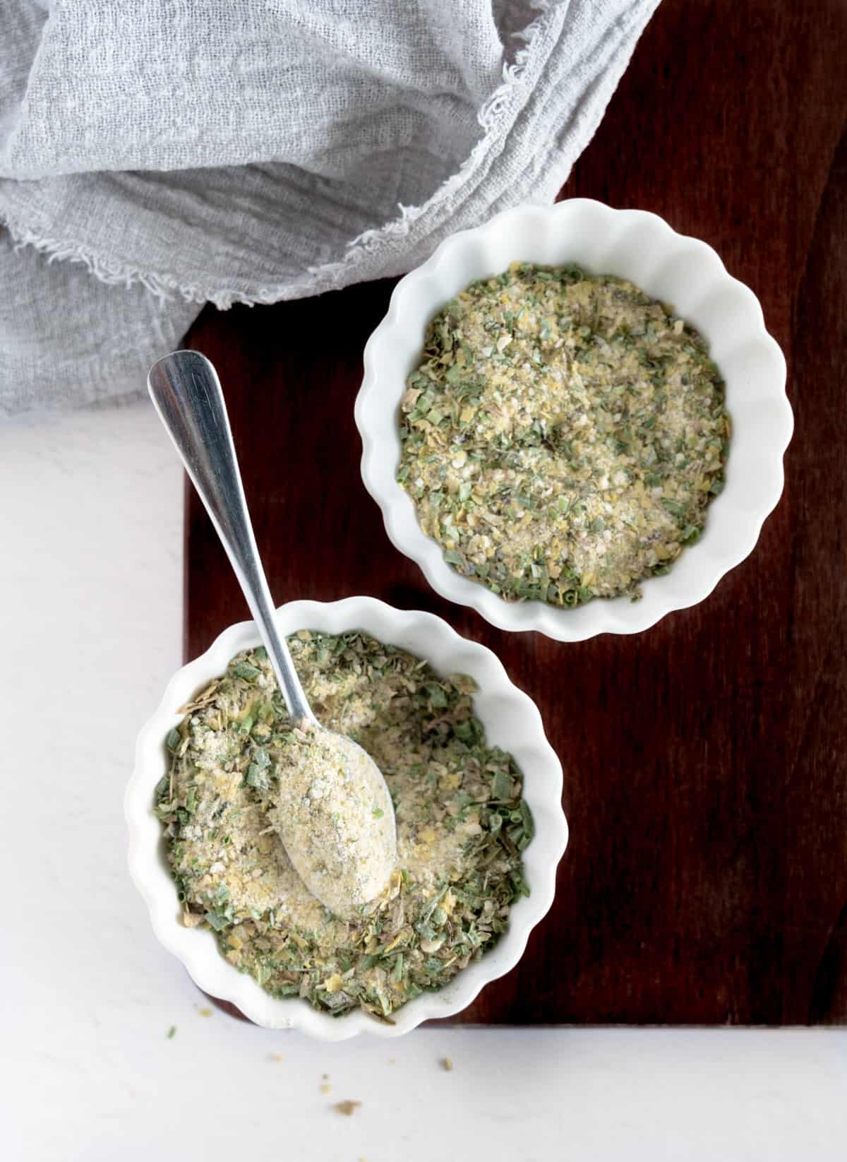 two white bowls with dried herbs mixed through a light yellow powder