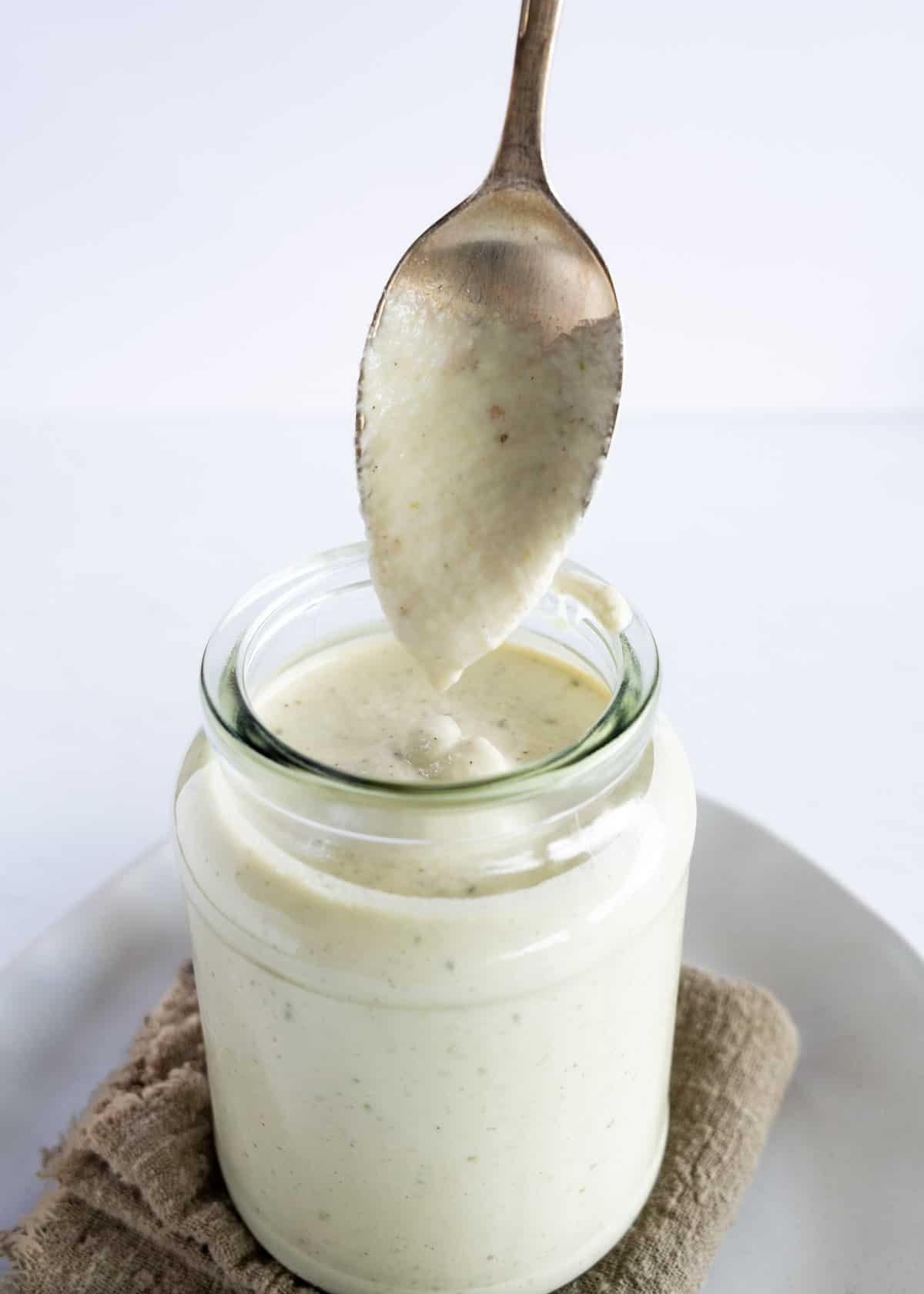 a glass jar filled with white sauce with a spoon dripping it in