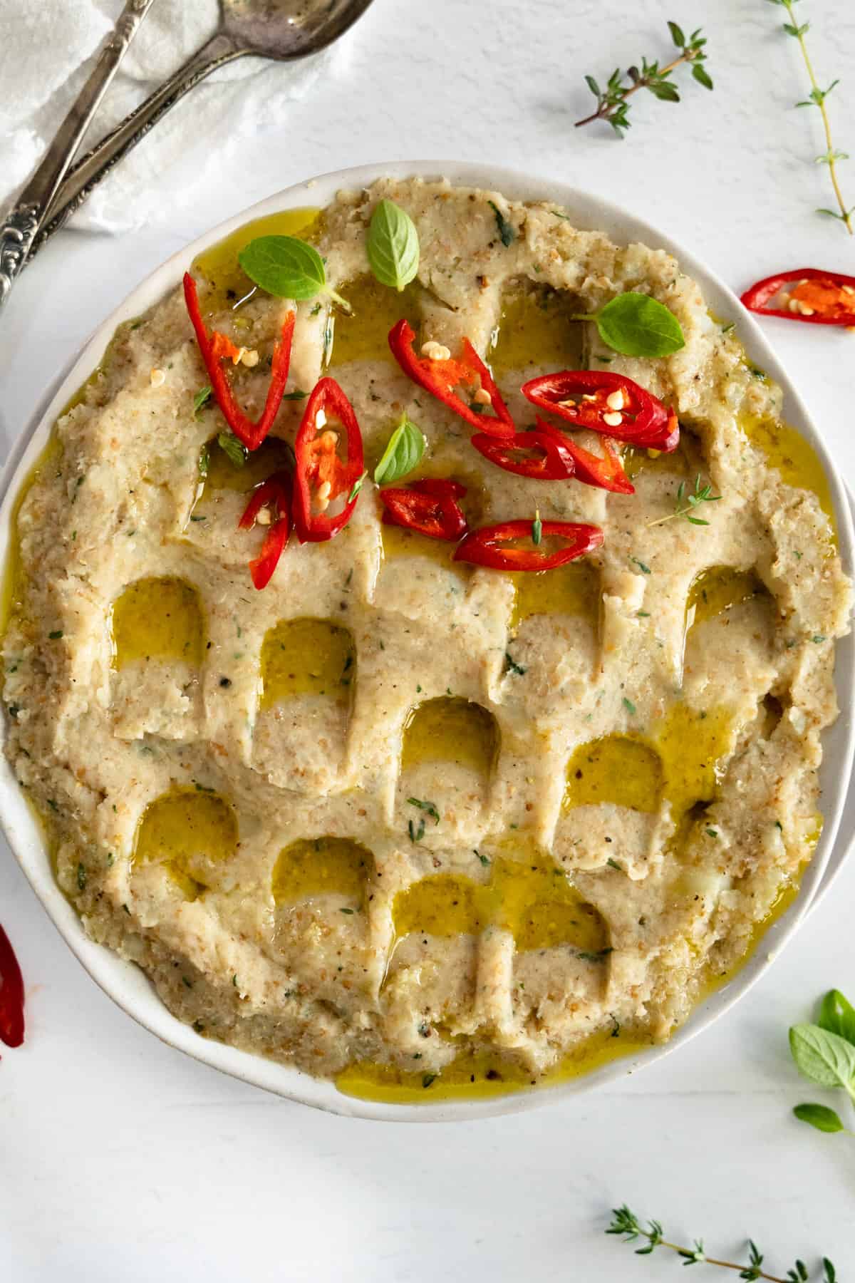 a white plate with mashed potato and bughul topped with olive oil and red chillies