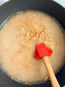 water added to a pot of bulgur and vermicelli with a red spoon