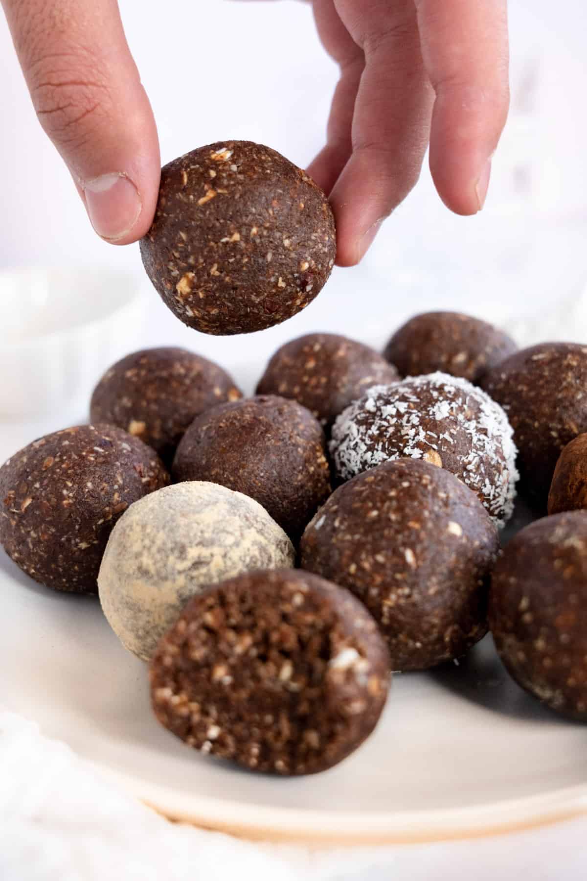 a male hand holding one chocolate ball on top of a plate full of them