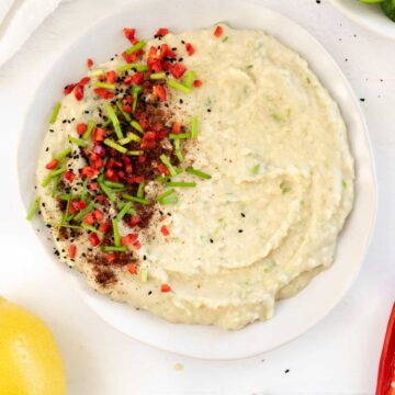 a white plate with white dip with green specks topped with red spices