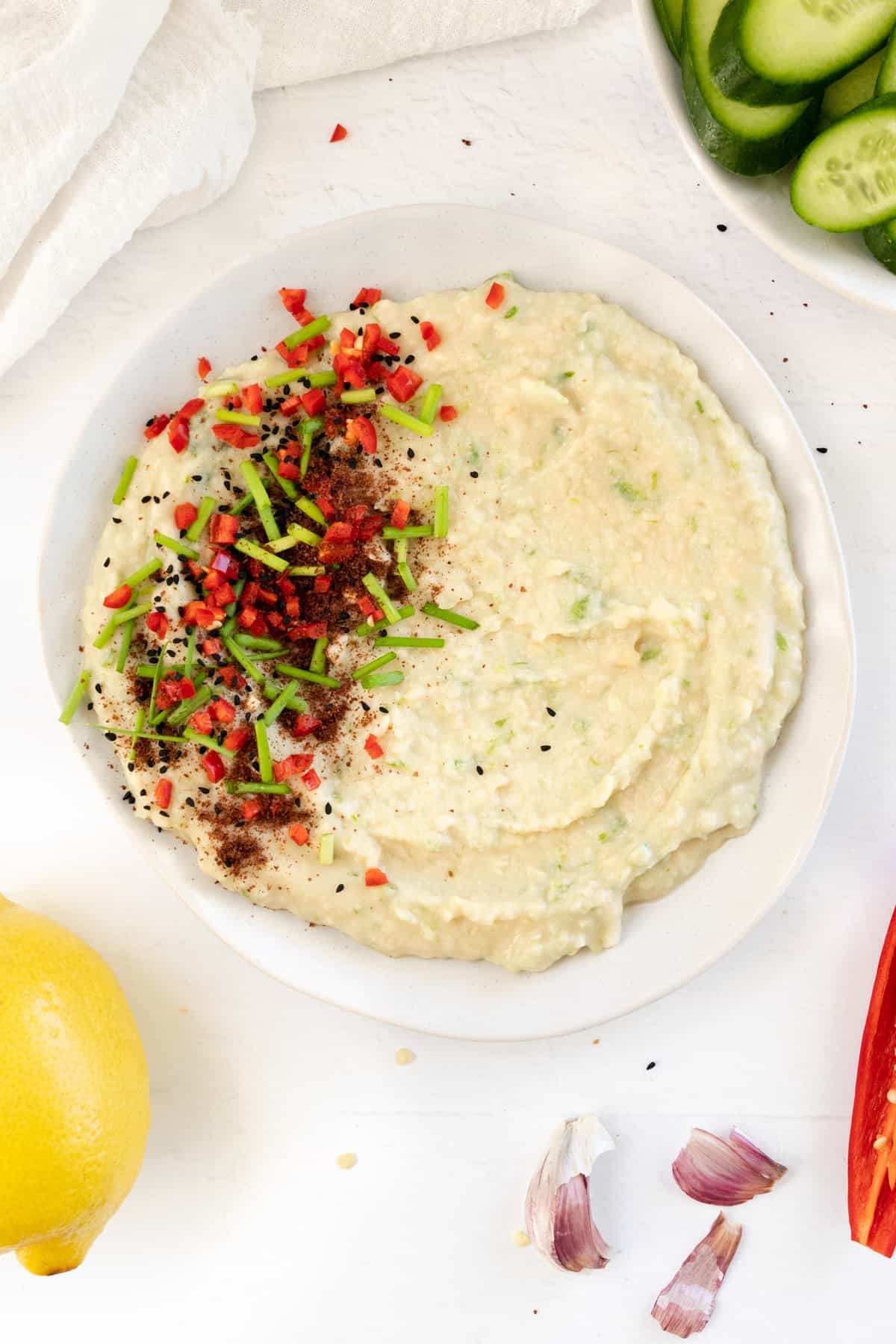 a white plate with white dip with green specks topped with red spices