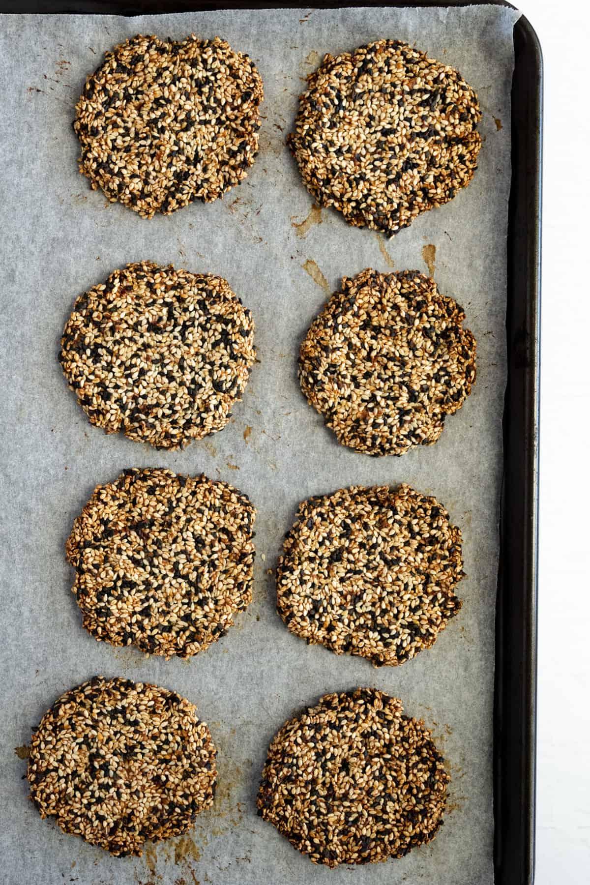 8 golden brown sesame seed cookies on a baking tray