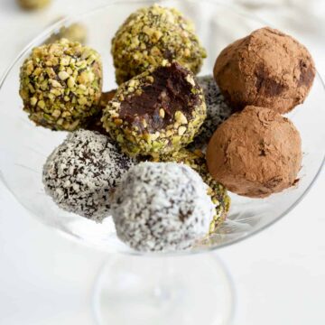 a champagne glass filled with chocolate date balls covered in either pistachio, cacao or coconut