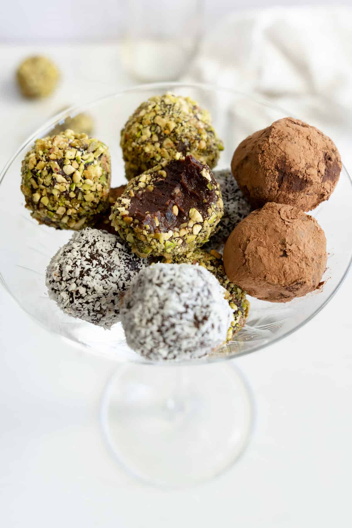 a champagn glass filled with chocolate date balls covered in either pistachio, cacao or coconut