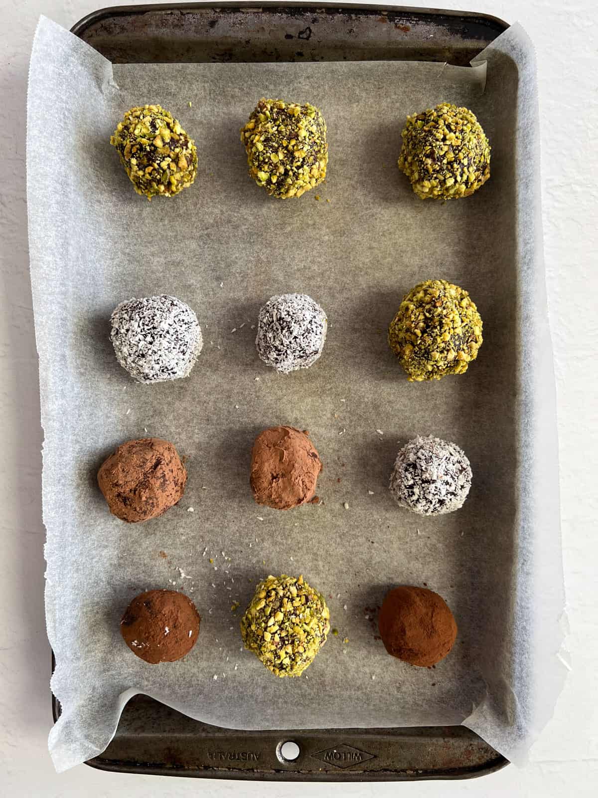 brown balls coated in either crushed pisatchio, desiccated coconut or cacao powder in a tray
