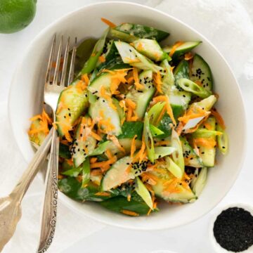 a bowl filled with chopped cucumber, grated carrots in a dressing