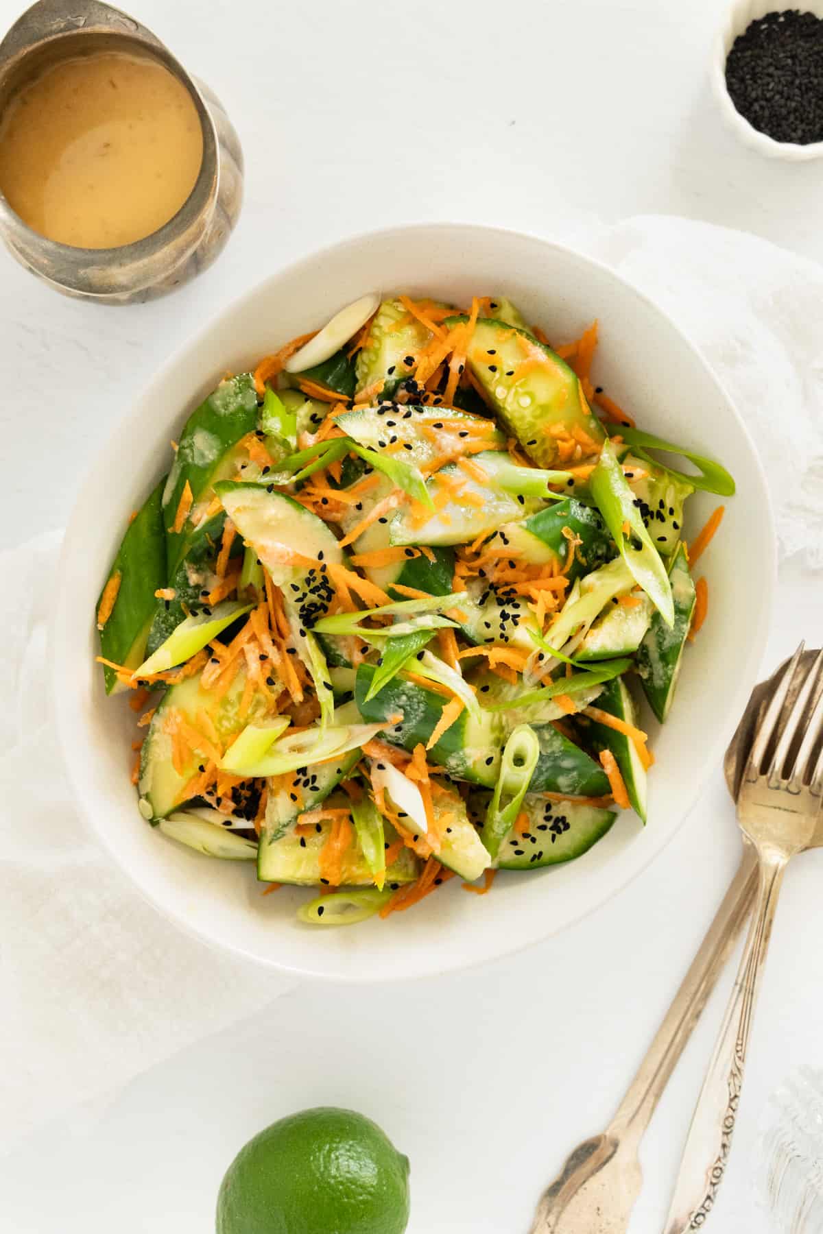 a bowl of green and orange salad with brownish tahini dressing on the side