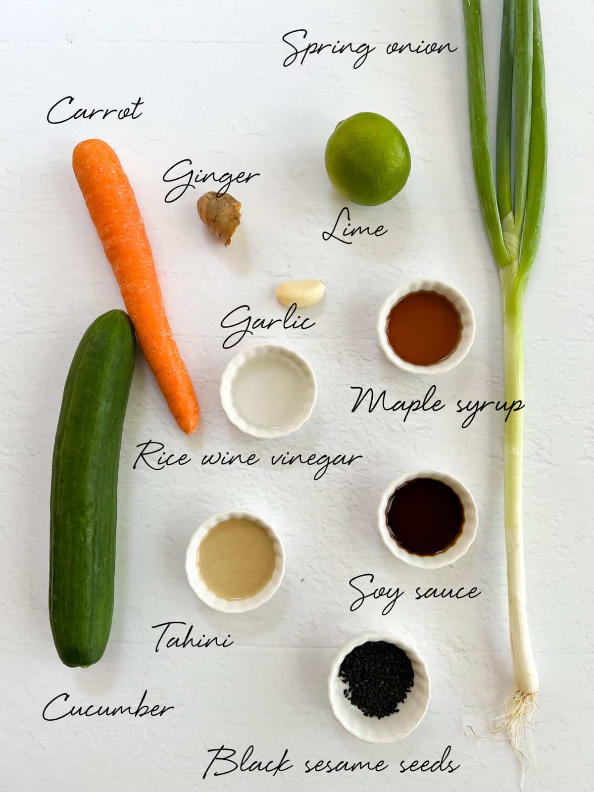 srping onion, carrot, cucumber, lime, ginger, garlic, tahini and sauces in white bowls on a white bench
