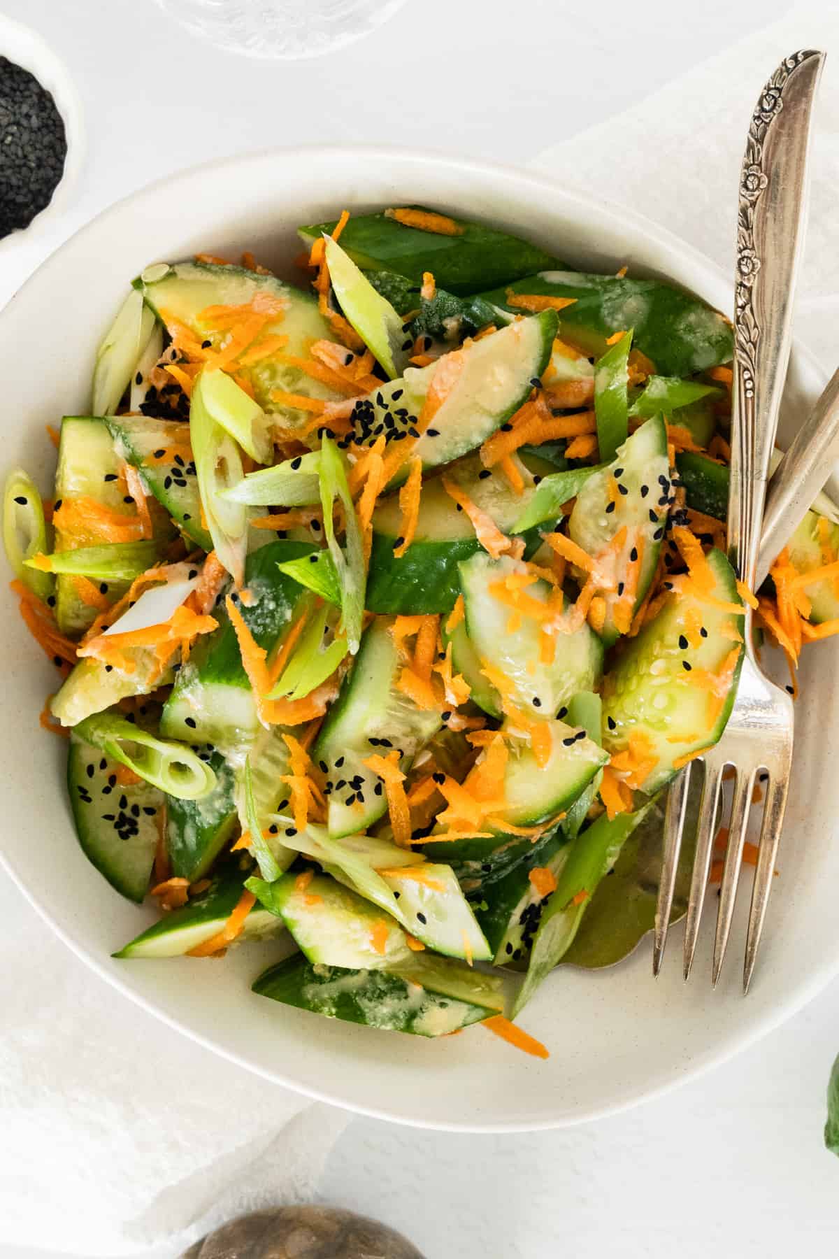 a white bowl filled with sliced cucumber carrot spring onion salad