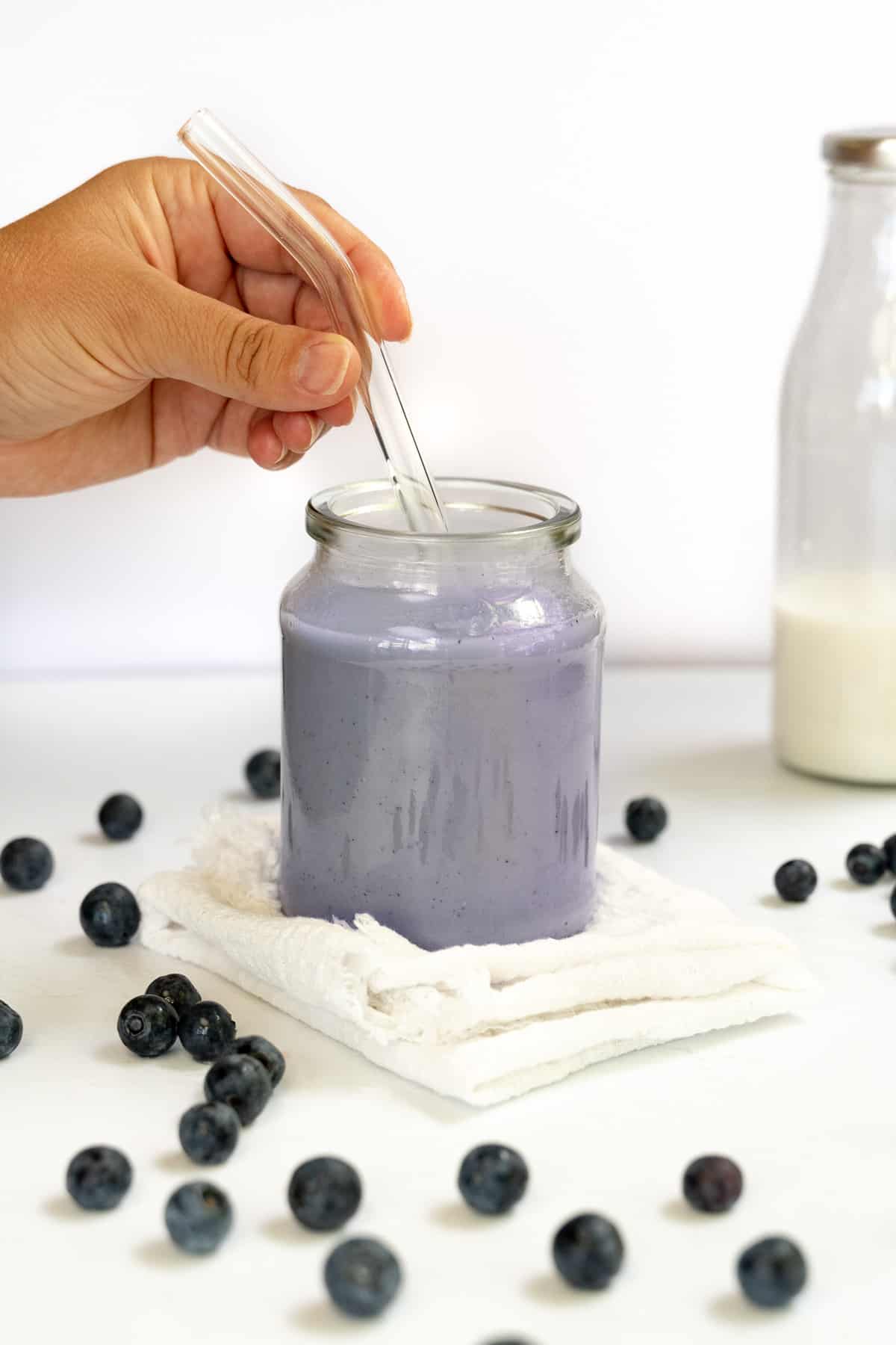 a hand holding a glass straw in a glass of purple mild