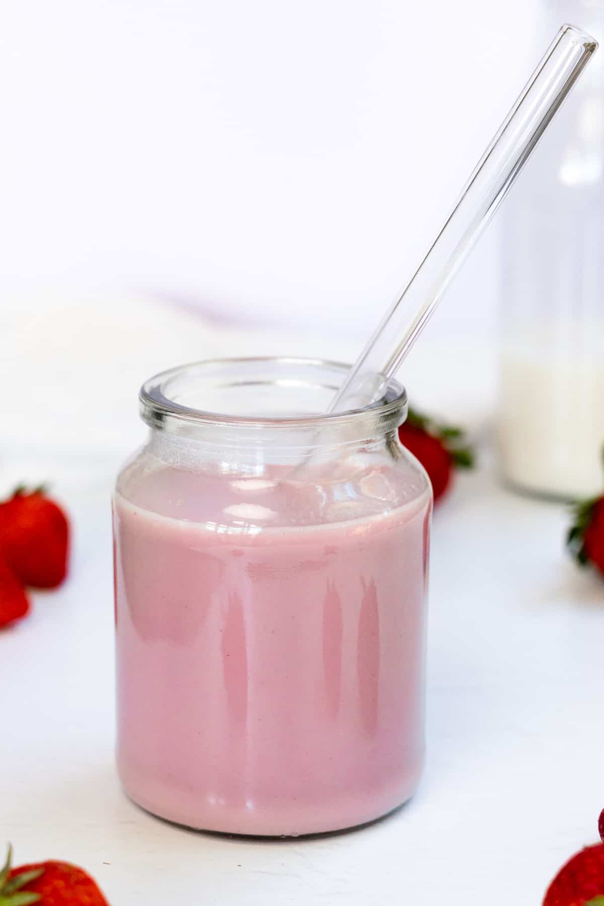 a glass cup with glass straw with pink milk in it