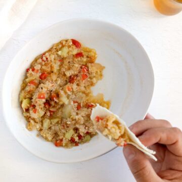 a white plate filled with cooked bulgur, zucchini flesh and red belle pepper with a hand holding some in a piece of bread