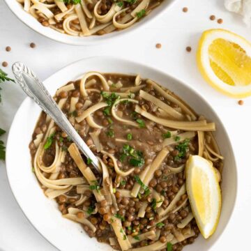a white bowl filled with a soup of pasta and lentils and a wedge of lemon