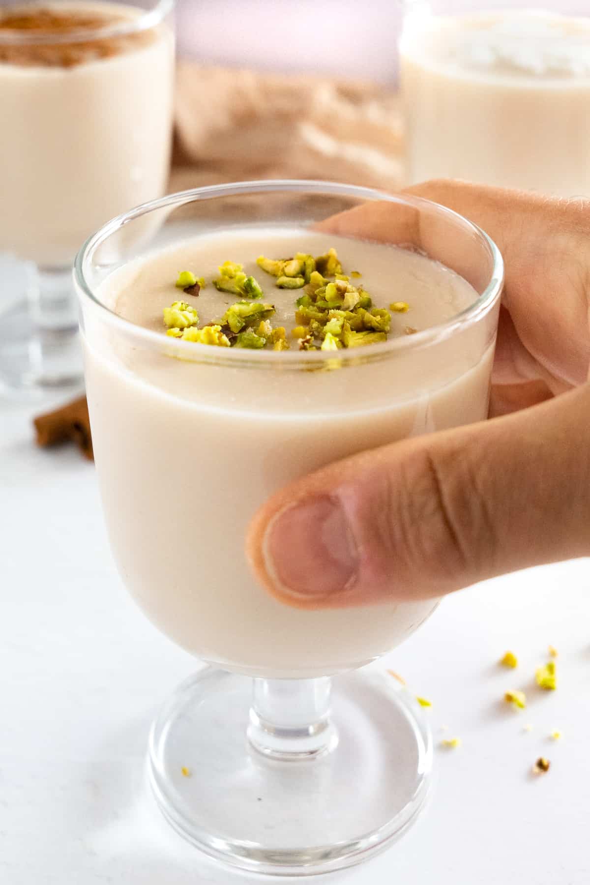 a mal hand holding a glass of thickened milk topped with crushed pistachio