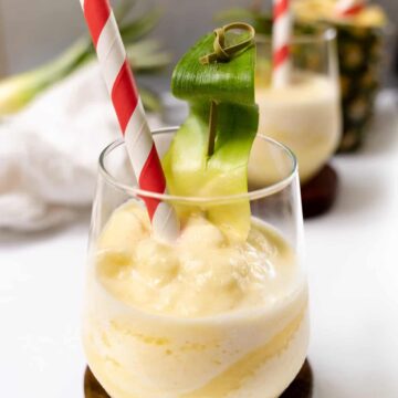 a glass cup with yellow frozen drink and a pineapple in the background