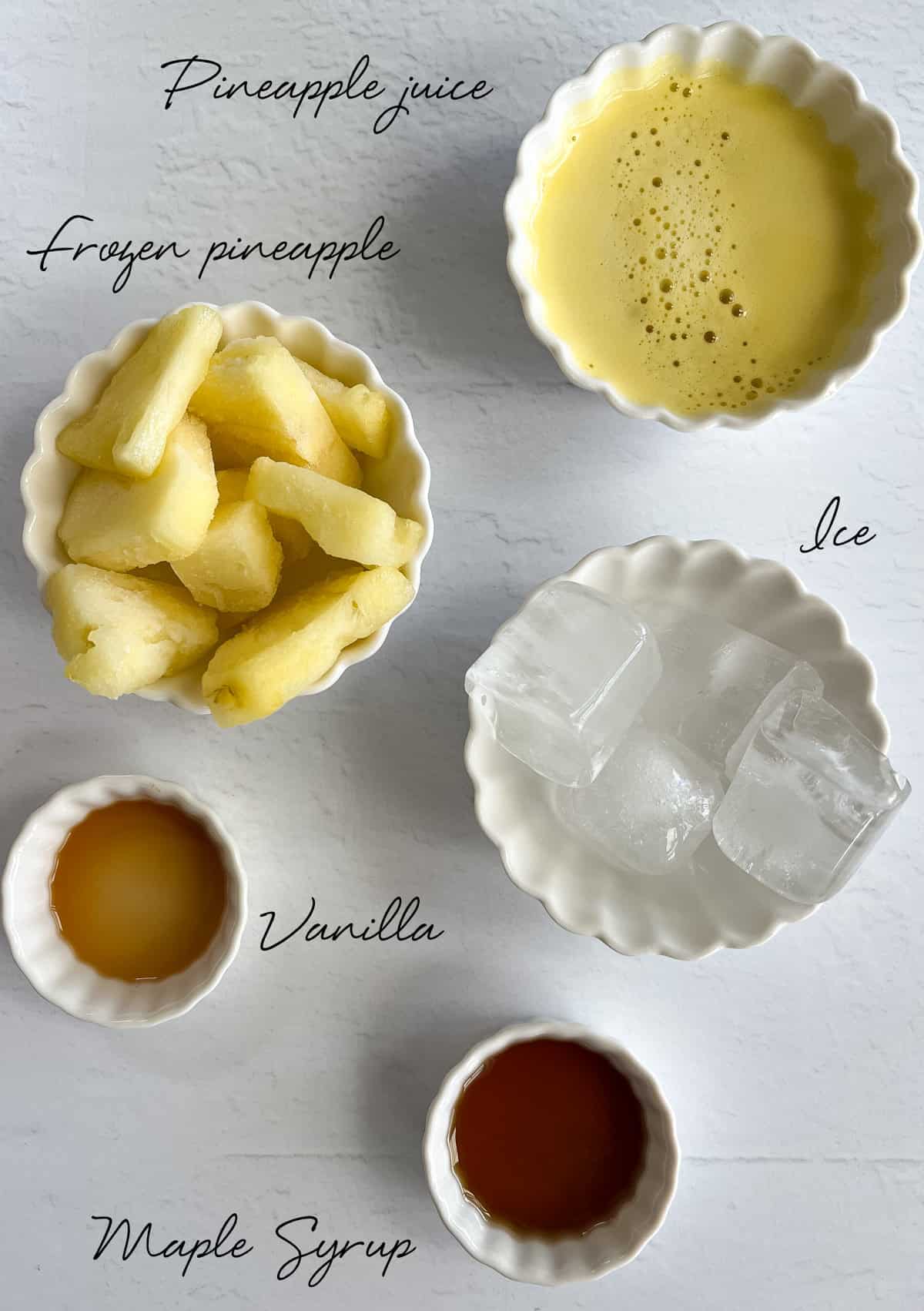 frozen pineapple pieces, pineapple juice, ice, maple syrup and vanilla in white bowls