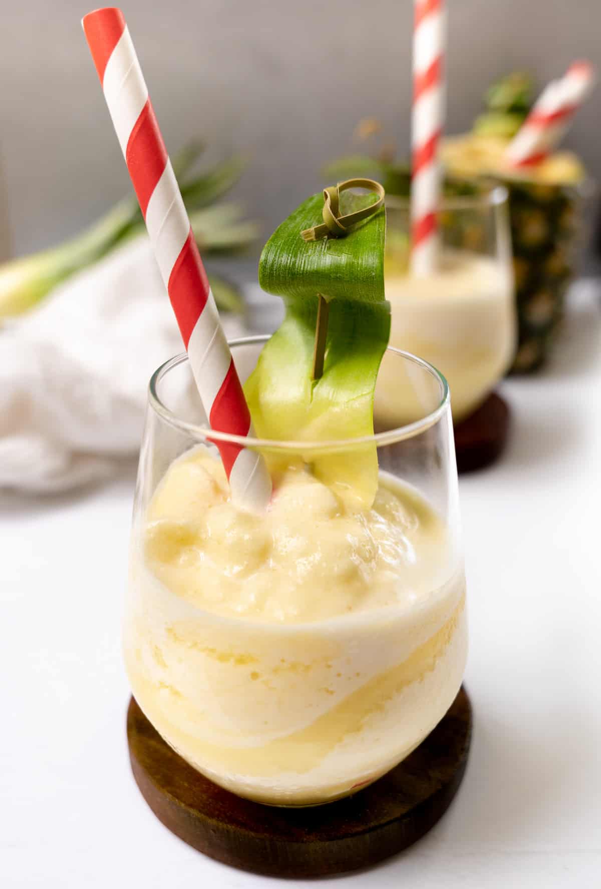 a glass cup with yellow frozen drink and a pineapple in the background